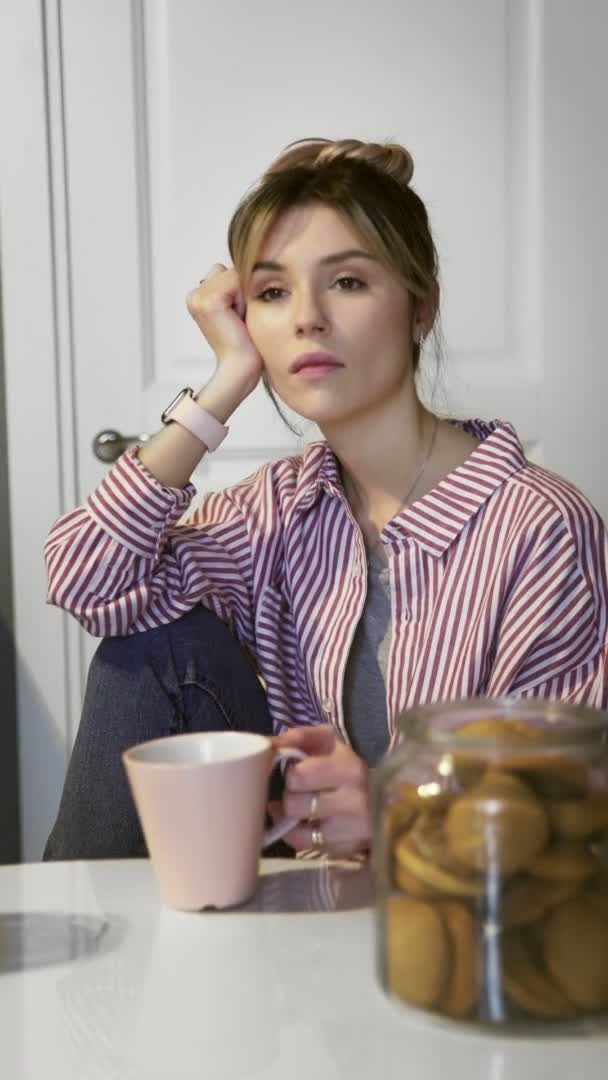 Vidéo verticale de jeune belle femme brune boit du café et mange des biscuits à la maison dans la cuisine — Video