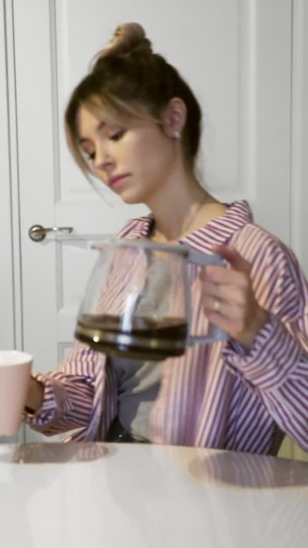 Вертикальное видео молодой красивой брюнетки женщина наливает и пьет кофе дома на кухне — стоковое видео