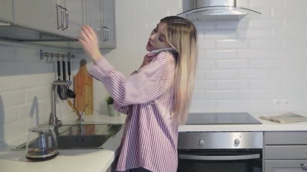 Függőleges videó fiatal gyönyörű nő iszik reggeli kávé a konyhában, és telefonon beszél — Stock videók