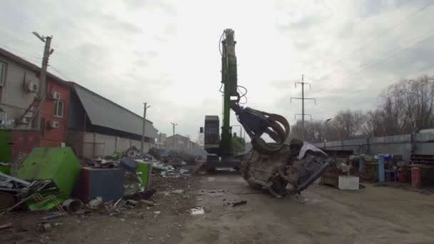 Machine with mechanical arm grabbing an old car from a pile at city landfill. — Stock Video