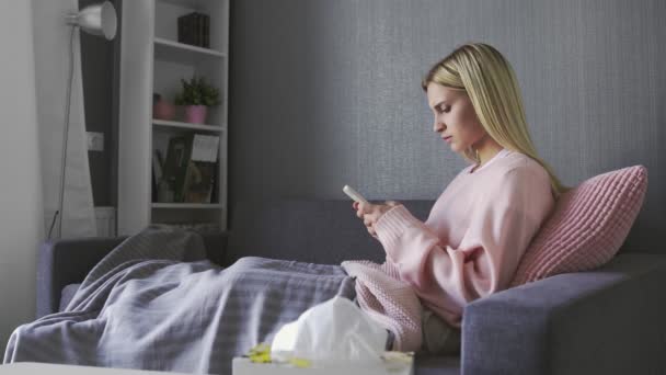 Overstuur jonge vrouw zit op de bank, houdt smartphone in de hand, ontvangen bericht met slecht nieuws. — Stockvideo