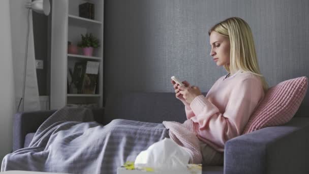 Smutna młoda kobieta czyta złe wieści i rzuca telefonem siedząc na kanapie w domu — Wideo stockowe