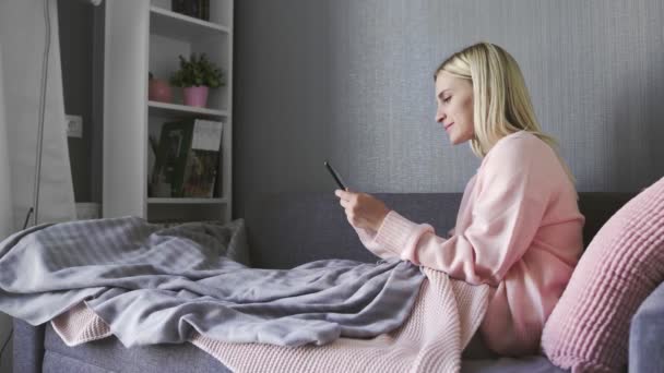 Mujer feliz viendo los medios de comunicación en la tableta sentada en un sofá en casa — Vídeos de Stock