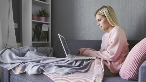 Молода жінка сидить на дивані за допомогою ноутбука, дивлячись на повідомлення на екрані — стокове відео