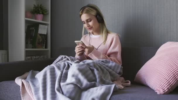 Jovem mulher usando fones de ouvido ouvindo música feliz segurando smartphone — Vídeo de Stock