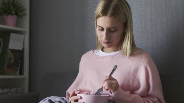 Jovem mulher senta-se no sofá e mantém tigela com salada — Vídeo de Stock