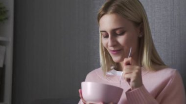 Genç bir kadın kanepeye oturur ve kaseden salata yer.