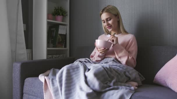 Ung kvinna sitter på soffan och äter sallad från skålen — Stockvideo