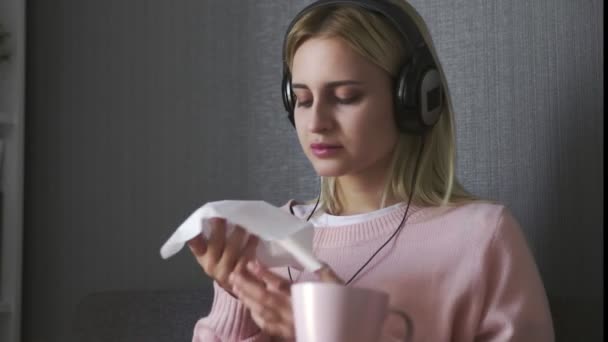 Zblízka mladá žena sedí na gauči jí toast s čokoládovou pomazánkou a poslouchat hudbu na smartphone — Stock video