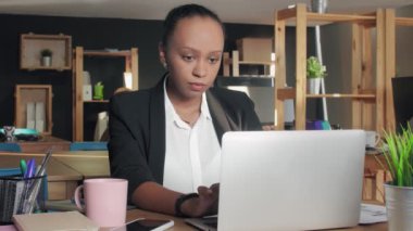Genç Afro-Amerikalı kadın laptopuyla ofisinde yazı yazıyor.