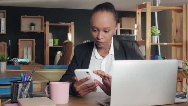 Jeune femme afro-américaine utilisant le téléphone en regardant l'écran surfer sur les médias sociaux au bureau — Video