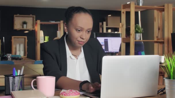 Mladá africká americká žena pracuje na notebooku a někdy se dívá na její koblihu
