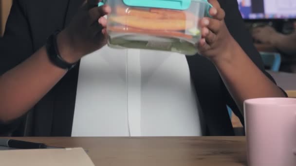 Close up of young african american woman having lunch at office. Woman eats vegetables from her container — Stock Video