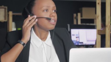 Kulaklıklı Afro-Amerikan bir kadının akıllı telefonuna bakıp gülerken bir müşteriyle konuşmasına yakından bakın.
