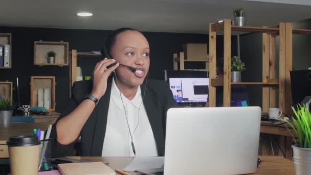 Mujer afroamericana enojada con auriculares habla con un cliente mientras mira el monitor de su computadora . — Vídeo de stock