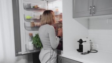 Kadın mutfaktaki buzdolabının kapısını açıyor ve salata yiyor.