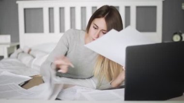 Ciddi kız öğrenci yatağa uzanıp ders çalışıyor.