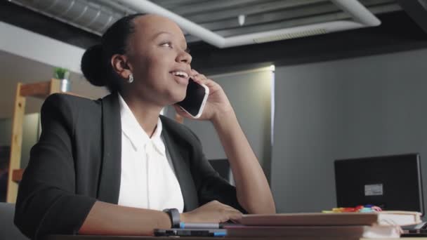 Vue latérale d'une jeune femme afro-américaine parlant au téléphone dans un bureau de coworking — Video