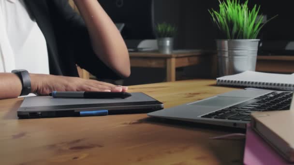 African american woman designer working at a laptop with a graphics tablet and drinking a coffee — Stock Video