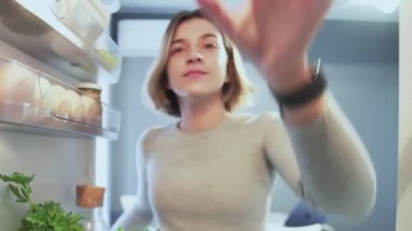 Buzdolabının içinden dışarı bakan kadın kapıyı açar ve bir elma alır.