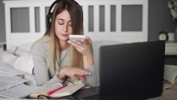 Mujer joven con auriculares tumbados en la cama y tomando una foto de su libro — Vídeo de stock