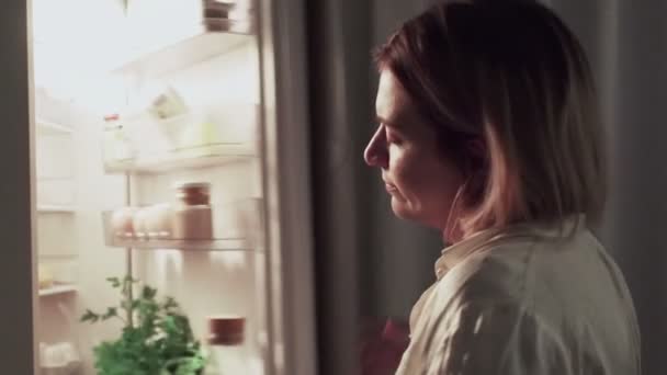 Mulher abre porta do frigorífico e leva salada, tarde da noite na cozinha — Vídeo de Stock
