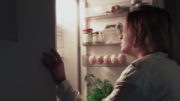 Žena otevře dveře ledničky pozdě v noci v kuchyni — Stock video