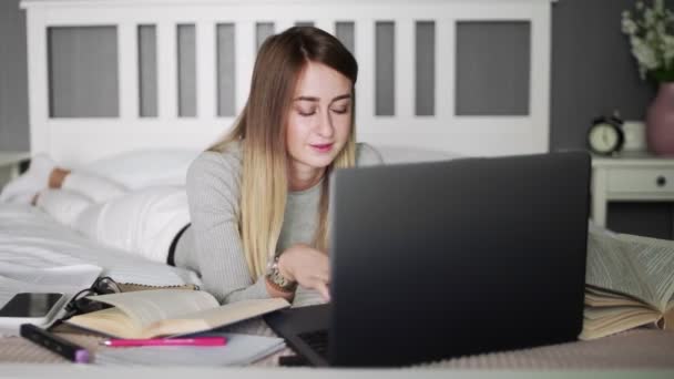 Junge Frau liegt auf dem Bett und tippt auf Notizbuch und Smartphone — Stockvideo