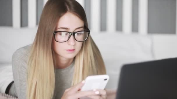 Fiatal nő galsess feküdt az ágyon, és használja okostelefon — Stock videók