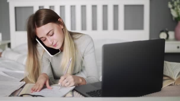 Young woman working at the home, she lying on the bed and talking on phone — Stock Video