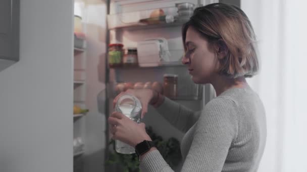 Közelkép a nő kinyitja a hűtőszekrény ajtaját a konyhában otthon, és vesz egy üveg tejet, majd önti a tejet az üveg — Stock videók