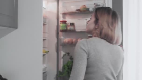 Vrouw opent koelkast deur in de keuken thuis en neemt appel — Stockvideo