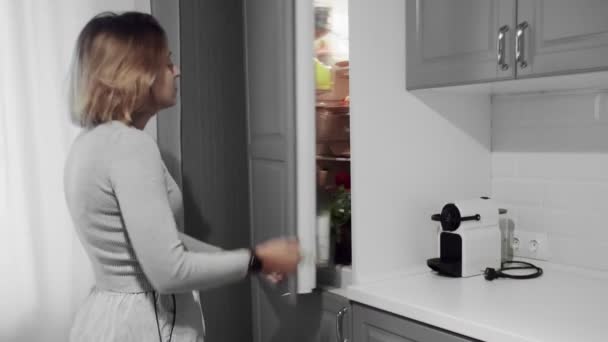 Vrouw opent koelkast deur in de keuken thuis en neemt appel — Stockvideo