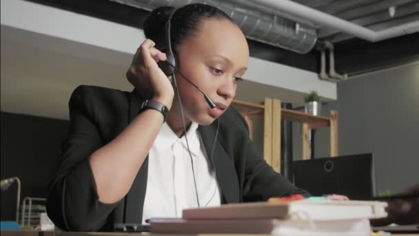 Down weergave van de jonge Afrikaanse Amerikaanse vrouw met headset gesprekken met een klant, terwijl het kijken naar haar computer monitor. — Stockvideo