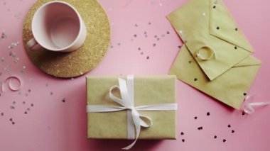 Kadın elleri beyaz kurdeleyle sarılı bir Noel hediyesini sallıyor. Tahta, pembe masa, düz uzanma.