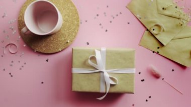 Kadın eli, beyaz kurdeleyle sarılmış bir Noel hediyesine dokunuyor. Tahta, pembe masa, düz uzanma.