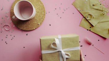 Kadın elleri, el sanatları kağıdına sarılmış beyaz kurdeleli Noel hediyesini ahşap masanın üstüne koyuyor.