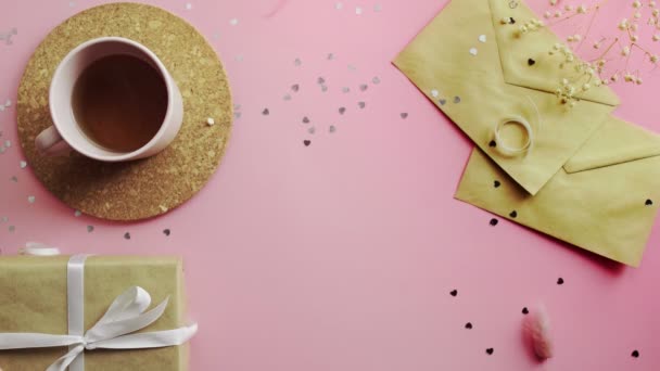 Mulher tirando uma foto plana. Vista superior sobre mesa rosa de madeira com dois concertos postais presentes em um papel artesanal e xícara de chá — Vídeo de Stock