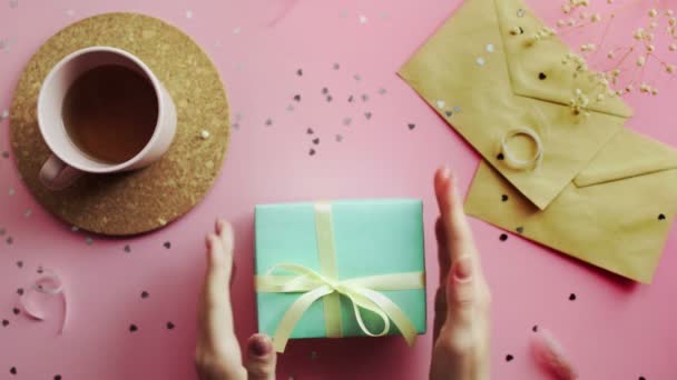 Eine Frau reicht ein in ein grünes Papier eingewickeltes Weihnachtsgeschenk mit gelber Schleife. Draufsicht auf holzrosa Tisch, flach gelegt — Stockvideo