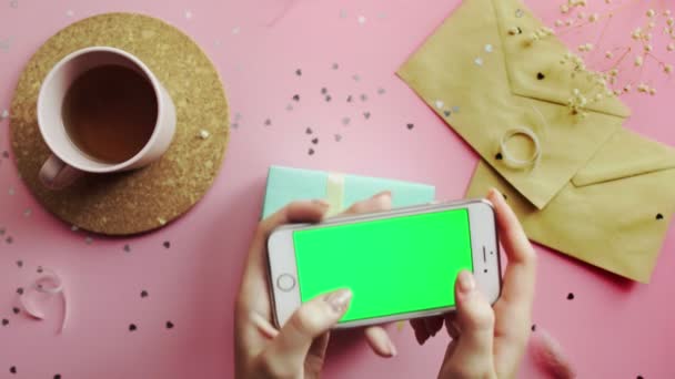 Vrouw maakt een foto van een kerstcadeau verpakt in een groen papier met gele strik. Bovenaanzicht op hout roze tafel, plat gelegd — Stockvideo