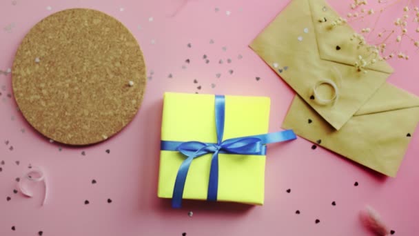 Mulher bebendo um chá e tomando um presente de Natal embrulhado em papel amarelo com arco azul. Vista superior sobre mesa rosa de madeira, flat lay — Vídeo de Stock