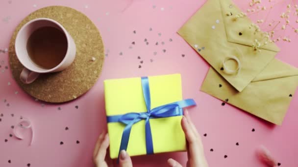 Női kéz vizsgálja a karácsonyi ajándék csomagolva sárga papír kék íj. Top kilátás a fa rózsaszín asztal, lapos laikus — Stock videók