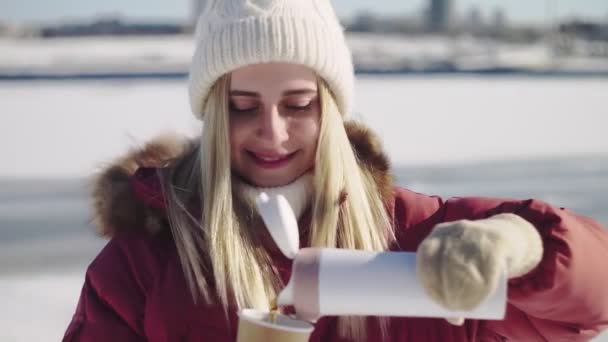 A woman pours tea fron thermos to cup in a snowy forest. A beautiful girl wants to warm herself in the winter outdoors with a mug of warm drink. Christmas Holidays — Stock Video