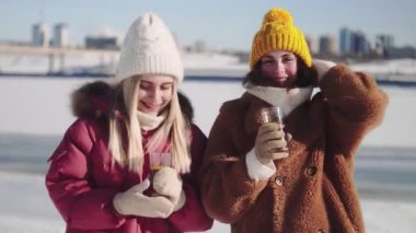 Örgü şapkalı iki genç kadın sıcak şarap ya da çay bardağıyla poz veriyor.