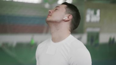Genç sporcu erkek kablosuz kulaklık takıyor ve spor öncesi esneme hareketleri yapıyor.