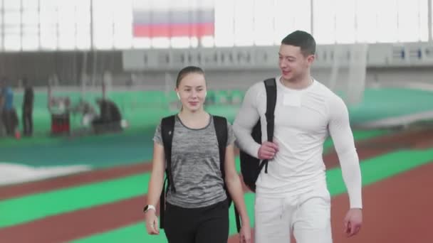 Jovem atlético casal corredor vem para arena desportiva e acenando as mãos para seus amigos — Vídeo de Stock
