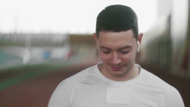 Молодий спортсмен чоловік з бездротовими навушниками дивиться на камеру — стокове відео