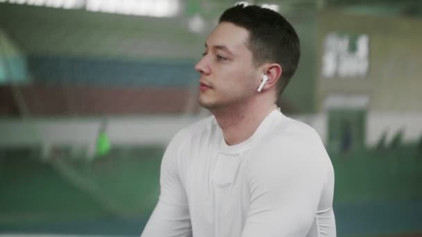 Joven atleta masculino con auriculares inalámbricos se calientan antes del ejercicio deportivo — Vídeo de stock