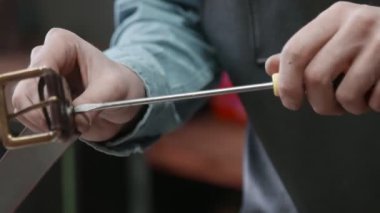 Önlüklü bir adam deri atölyesinde kahverengi deri kemer yapmak için tornavida kullanıyor. Deri atölyedeki deri kemerin çalışma süreci..