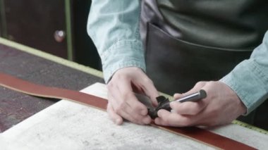 Tanner kemer için deri keser. Deri atölyedeki deri kemerin çalışma süreci. Adam el işi aleti tutuyor ve çalışıyor. Tanner eski tabakhanede..